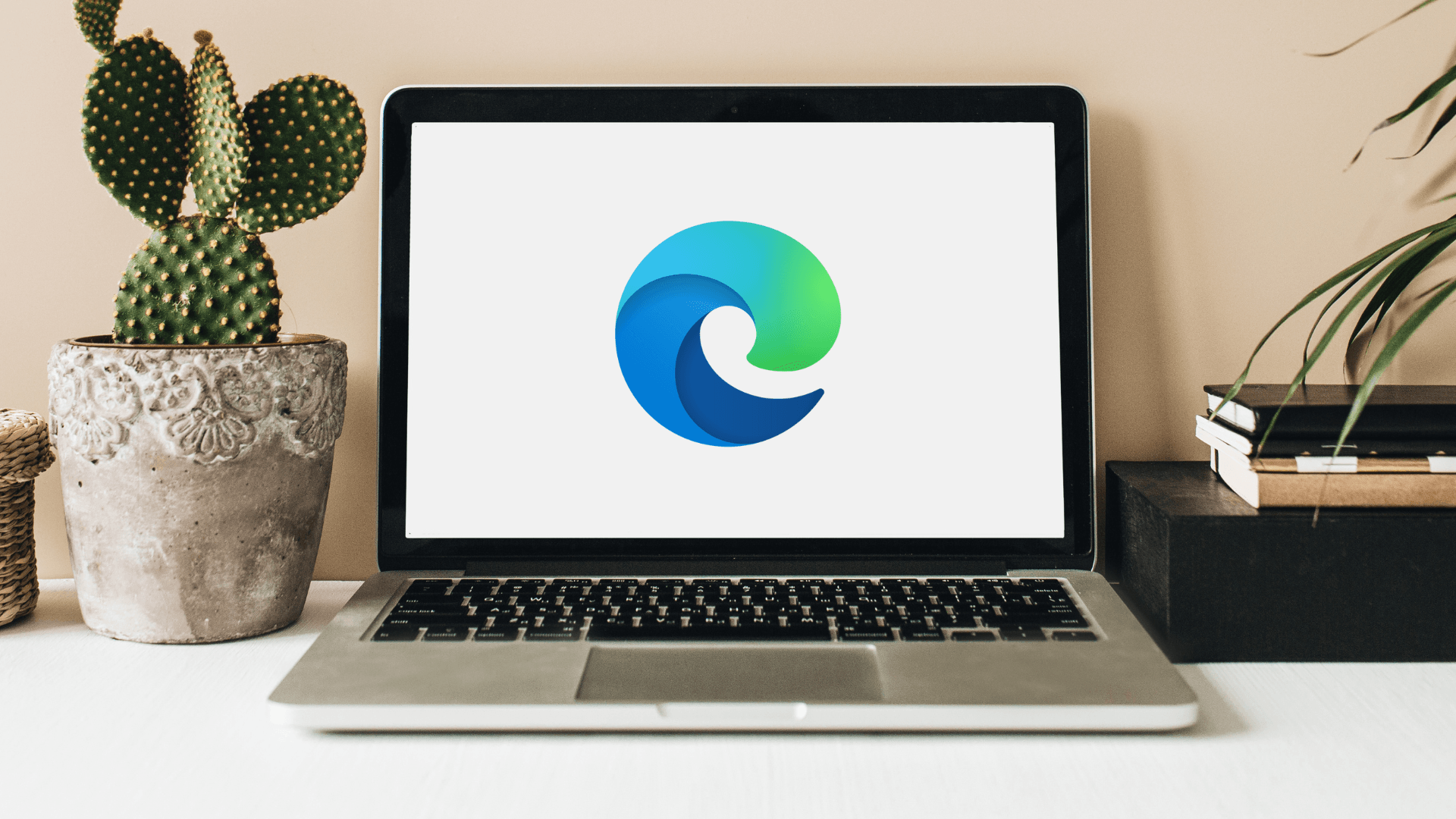 Laptop on desk displaying Microsoft Edge logo, flanked by a potted cactus and books, relating to the best browser for Windows 11.