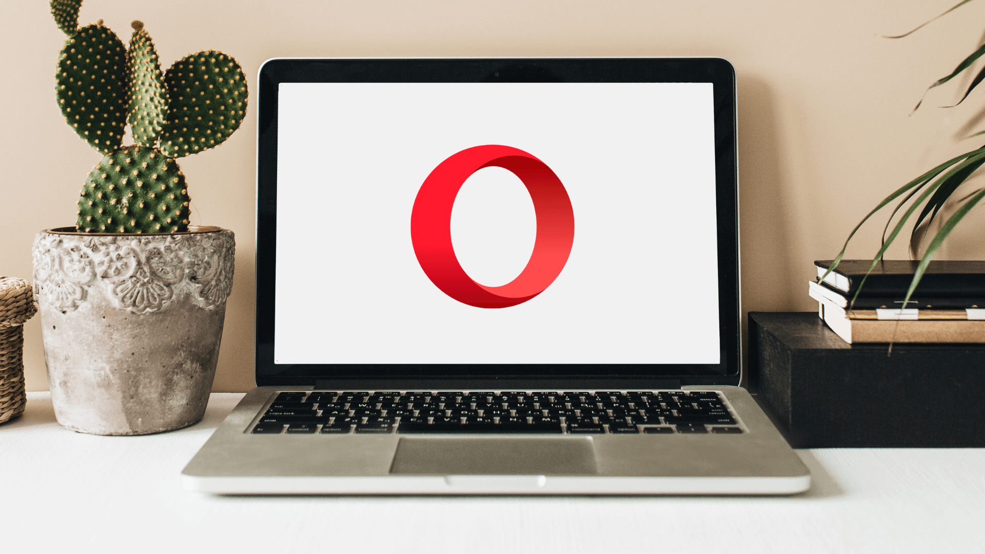 Laptop on desk with the Opera browser logo on screen, flanked by plants and books, relating to the best browser for Windows 11.