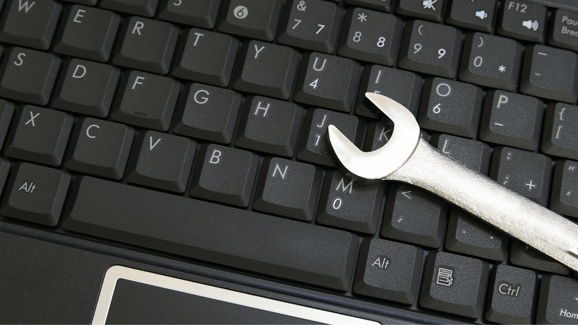 A wrench lying on a black computer keyboard.